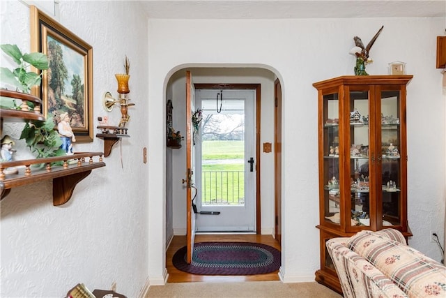 doorway with arched walkways, a textured wall, and baseboards