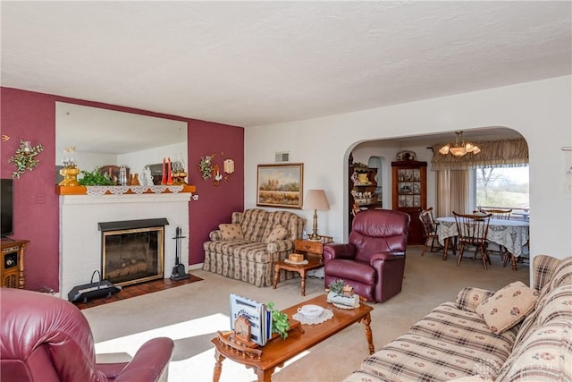 carpeted living area with a brick fireplace, arched walkways, an inviting chandelier, and visible vents
