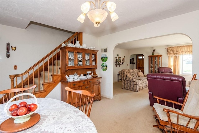 carpeted dining room featuring stairway, arched walkways, visible vents, and a chandelier