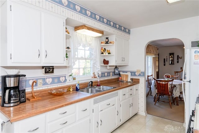 kitchen with freestanding refrigerator, arched walkways, open shelves, and a sink