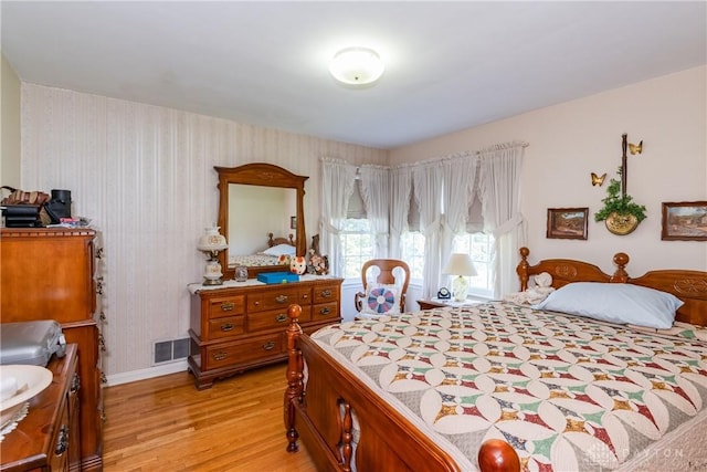 bedroom with baseboards, wallpapered walls, light wood-type flooring, and visible vents