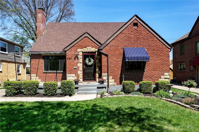 view of front of house featuring brick siding, a chimney, roof with shingles, and a front lawn