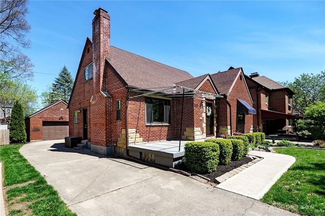 view of front of house featuring a garage, roof with shingles, a chimney, brick siding, and an outbuilding