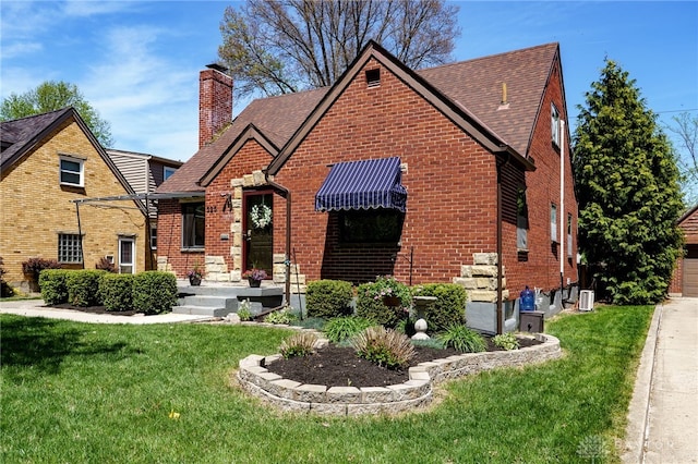 tudor-style house featuring brick siding, a shingled roof, and a front yard
