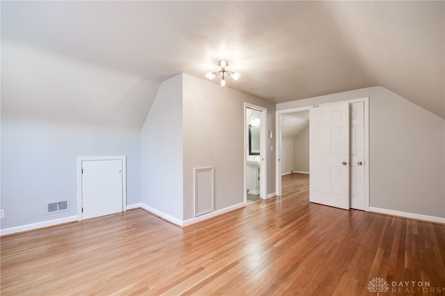 additional living space with baseboards, visible vents, light wood-style flooring, and lofted ceiling