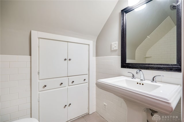 bathroom with tile walls, a sink, lofted ceiling, and a wainscoted wall
