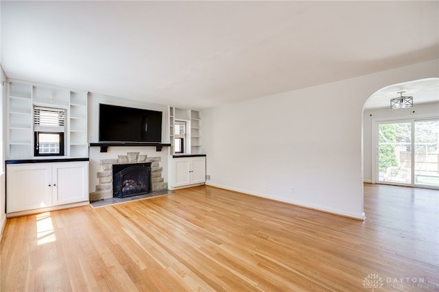 unfurnished living room with baseboards, arched walkways, light wood-style flooring, and a fireplace