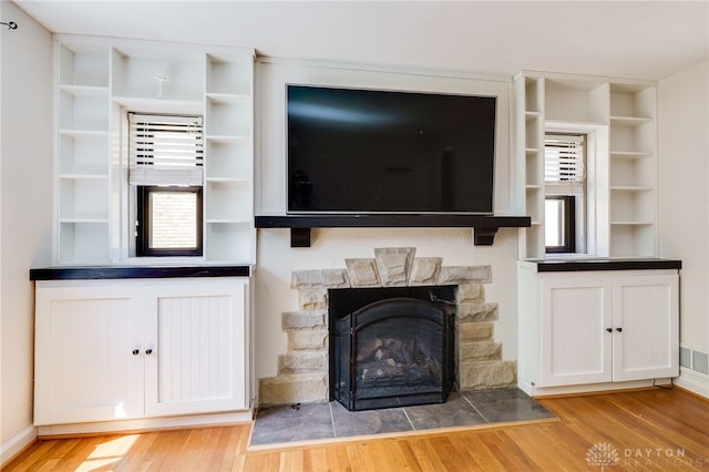 unfurnished living room with built in features, wood finished floors, and a fireplace