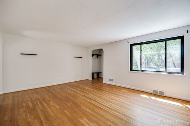 empty room featuring visible vents, arched walkways, light wood-style flooring, and baseboards