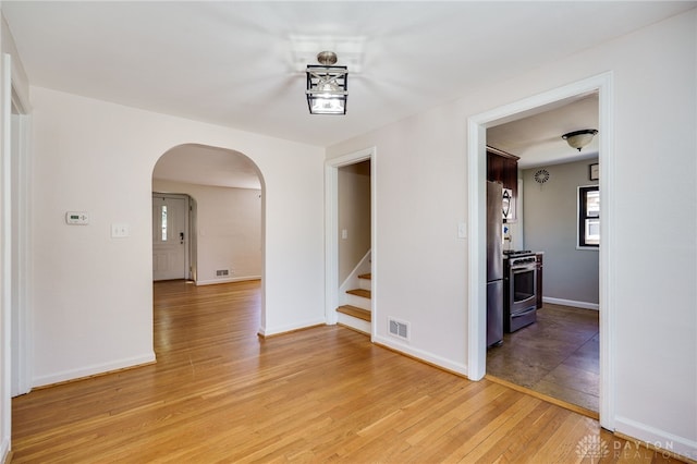 unfurnished room with arched walkways, light wood-style flooring, stairs, baseboards, and visible vents