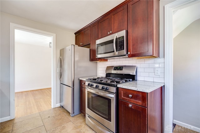 kitchen featuring reddish brown cabinets, baseboards, appliances with stainless steel finishes, and tasteful backsplash