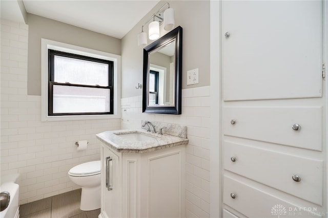 bathroom with wainscoting, vanity, toilet, tile patterned floors, and tile walls