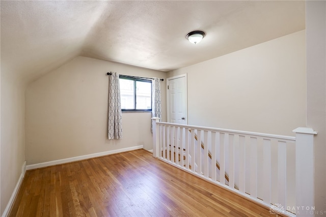 bonus room with a textured ceiling, baseboards, vaulted ceiling, and wood finished floors