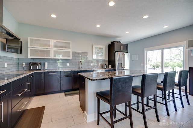 kitchen with high end refrigerator, stone countertops, a breakfast bar, and black electric stovetop