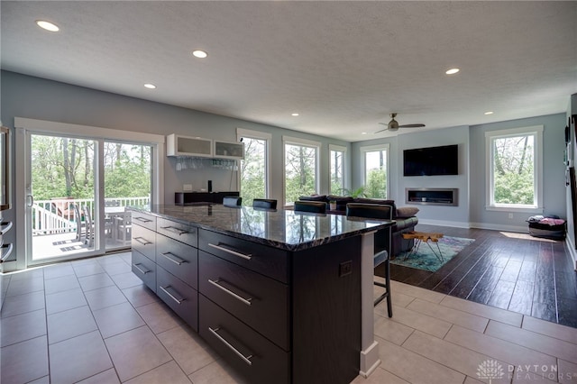kitchen featuring a kitchen island, a breakfast bar area, recessed lighting, a ceiling fan, and dark stone countertops