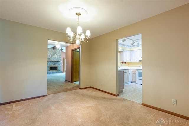 spare room with baseboards, a fireplace, a notable chandelier, and light carpet