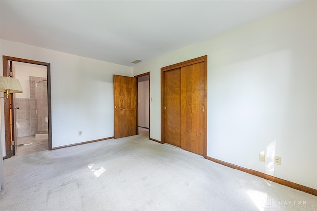 unfurnished bedroom featuring a closet, baseboards, ensuite bath, and light colored carpet