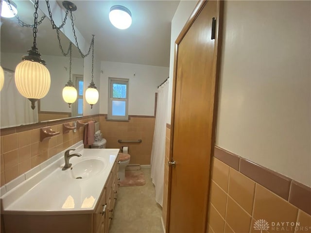 bathroom featuring tile walls, wainscoting, curtained shower, vanity, and toilet
