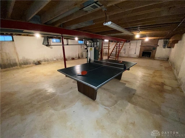 recreation room featuring water heater, visible vents, unfinished concrete floors, and a fireplace