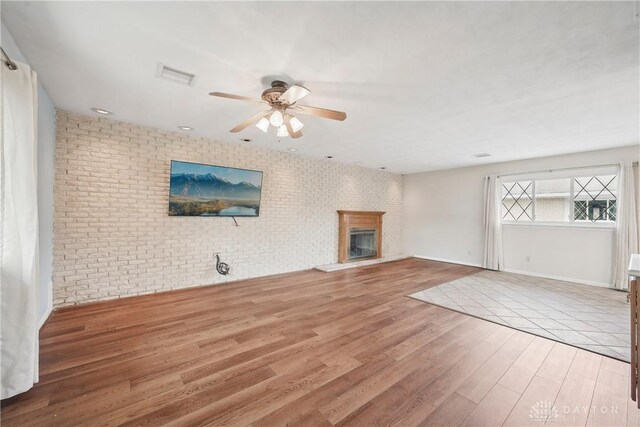 871 Van Eaton Rd, Spring Valley Twp, OH 45385 - unfurnished living room with a ceiling fan, brick wall, visible vents, wood finished floors, and a glass covered fireplace