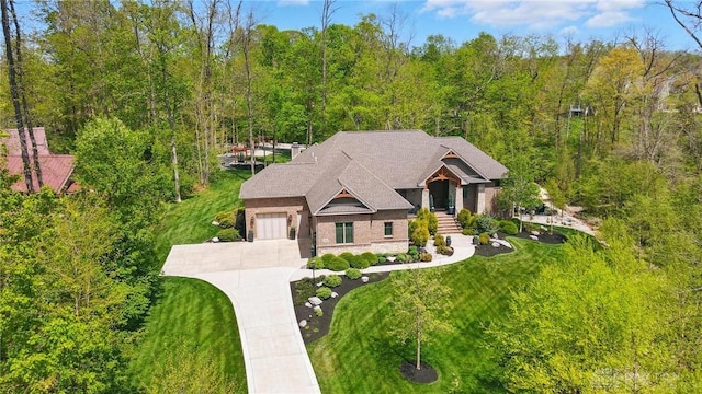 view of front of house featuring concrete driveway, an attached garage, a view of trees, and a front lawn