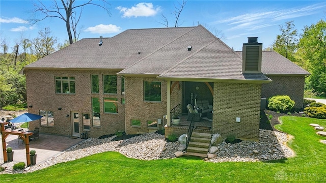 back of house with a chimney, a lawn, brick siding, a patio, and a shingled roof