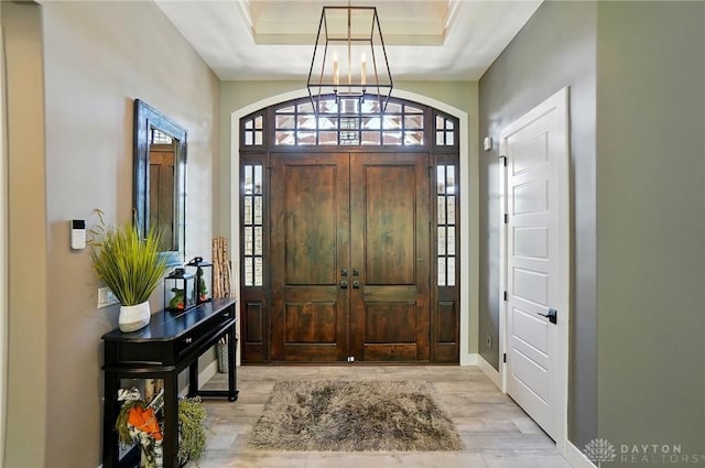 foyer entrance with light wood-type flooring, a tray ceiling, and a notable chandelier