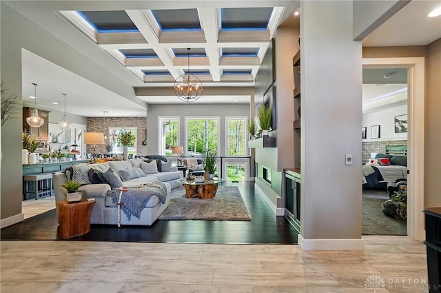 living room featuring an inviting chandelier, beam ceiling, a brick fireplace, hardwood / wood-style floors, and coffered ceiling