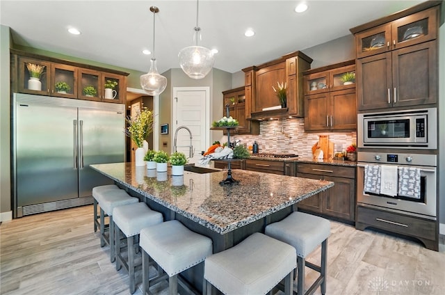 kitchen featuring tasteful backsplash, a sink, light wood-style floors, built in appliances, and a breakfast bar