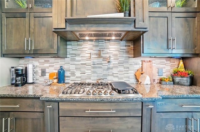 kitchen with light stone countertops, glass insert cabinets, stainless steel gas stovetop, and tasteful backsplash