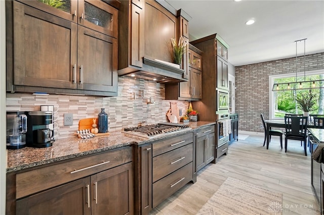 kitchen with decorative backsplash, brick wall, glass insert cabinets, stone countertops, and appliances with stainless steel finishes