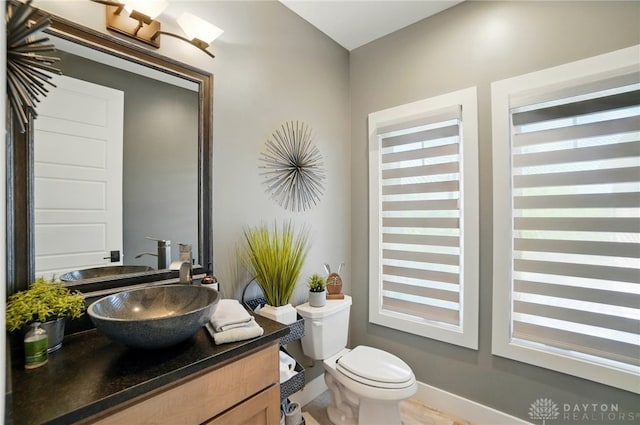half bathroom featuring toilet, baseboards, and vanity