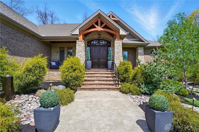 entrance to property featuring roof with shingles and stone siding