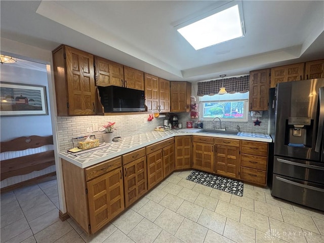 kitchen with black microwave, a tray ceiling, stainless steel fridge with ice dispenser, a sink, and backsplash