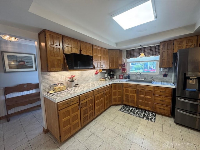 kitchen with tasteful backsplash, light countertops, a sink, black appliances, and a tray ceiling