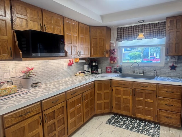 kitchen featuring light countertops, black microwave, brown cabinetry, and a sink