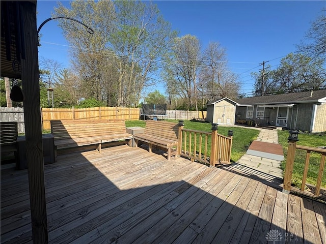deck featuring a trampoline, a lawn, a fenced backyard, an outdoor structure, and a shed