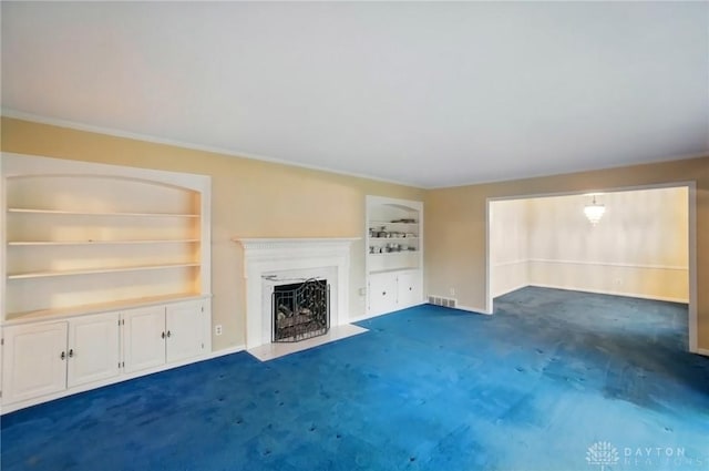 unfurnished living room with visible vents, ornamental molding, built in features, dark colored carpet, and a fireplace with flush hearth