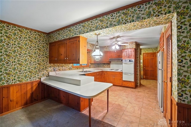 kitchen featuring wainscoting, light countertops, a peninsula, wallpapered walls, and ornamental molding