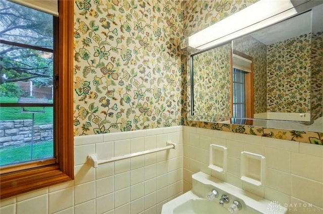 bathroom with wallpapered walls, tile walls, a sink, and a wainscoted wall