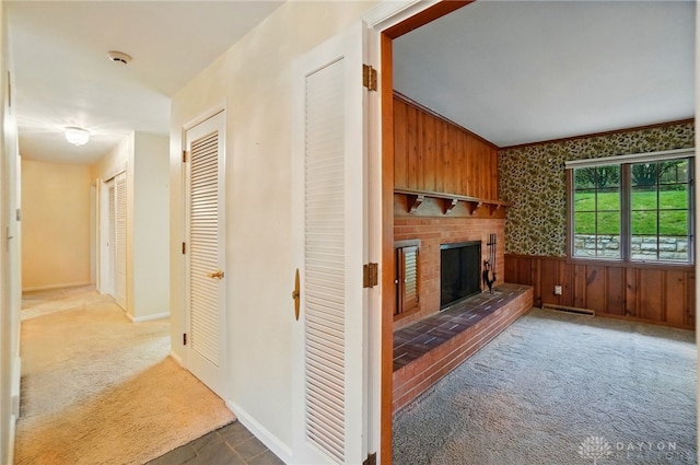 unfurnished living room featuring wooden walls, wainscoting, a fireplace, carpet floors, and baseboards