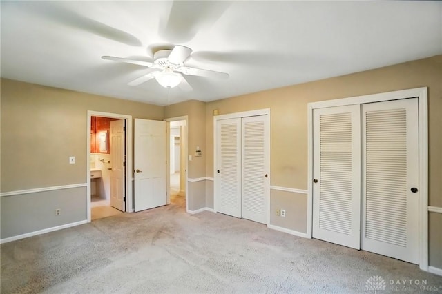 unfurnished bedroom featuring a ceiling fan, baseboards, two closets, carpet, and ensuite bath