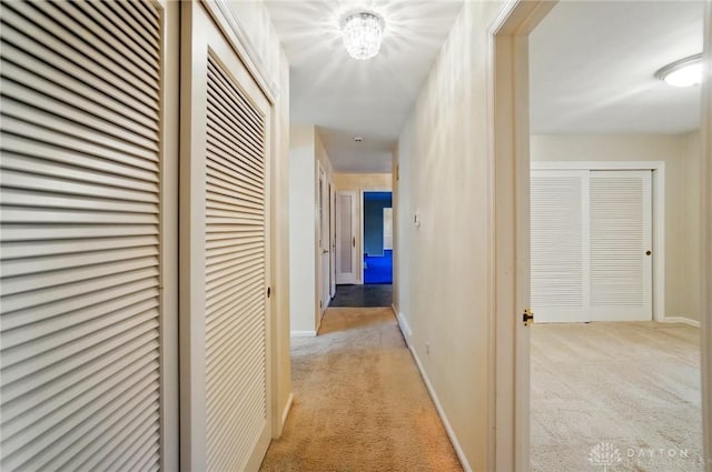 hallway featuring baseboards and light carpet