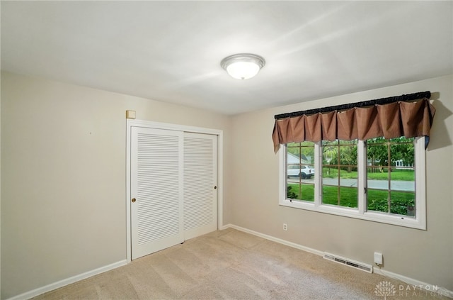 unfurnished bedroom featuring visible vents, baseboards, a closet, and light colored carpet