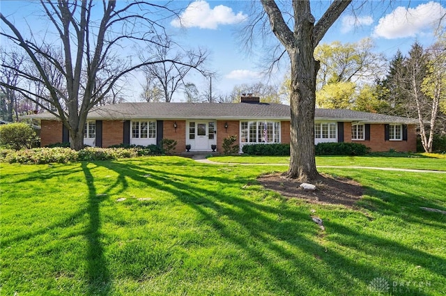 ranch-style home with brick siding, a front yard, and a chimney