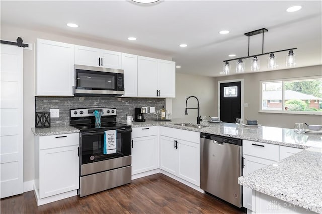 kitchen featuring appliances with stainless steel finishes, a sink, a peninsula, white cabinetry, and dark wood-type flooring