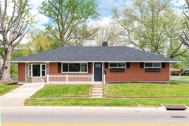 ranch-style home featuring a shingled roof, a front lawn, brick siding, a chimney, and covered porch