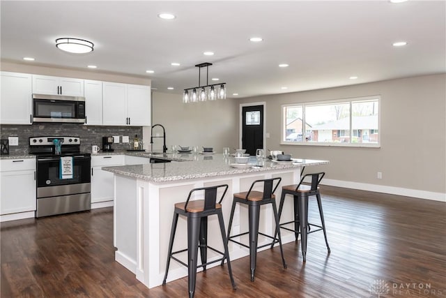 kitchen with decorative backsplash, a kitchen bar, dark wood-type flooring, white cabinetry, and appliances with stainless steel finishes