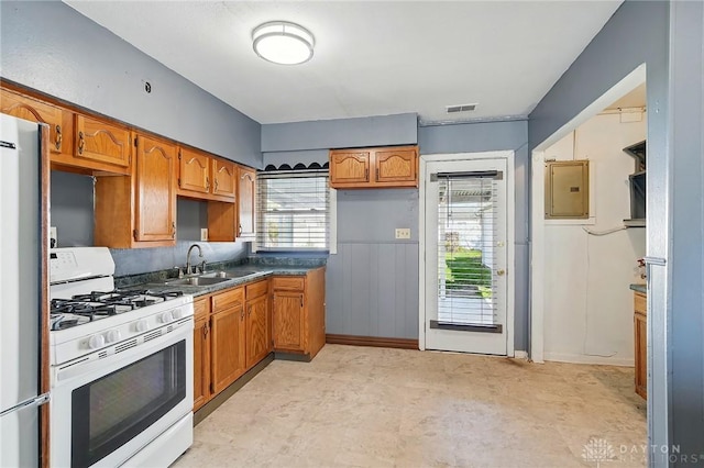 kitchen featuring electric panel, visible vents, brown cabinets, a sink, and white range with gas cooktop