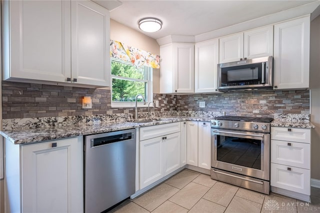 kitchen with decorative backsplash, light stone countertops, white cabinets, a sink, and appliances with stainless steel finishes